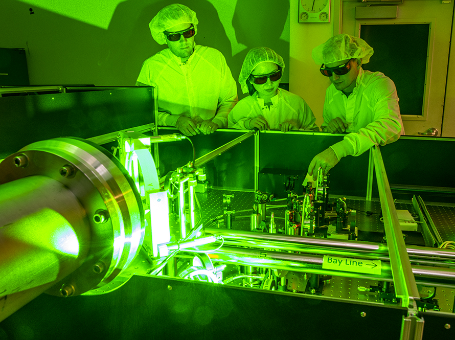Researchers work in Berkeley Lab Laser Accelerator Center at optical table amid green laser beams