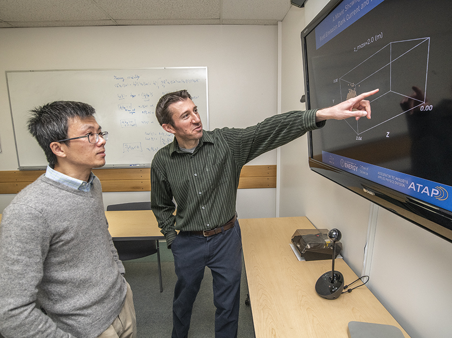 Two scientists discuss computer modeling output that is on a large wall mounted display