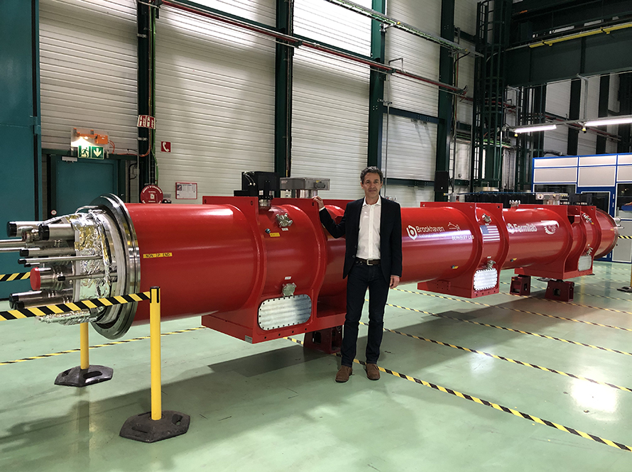 Scientist stands next to red-painted magnet 4.2 m long in a high-bay assembly building