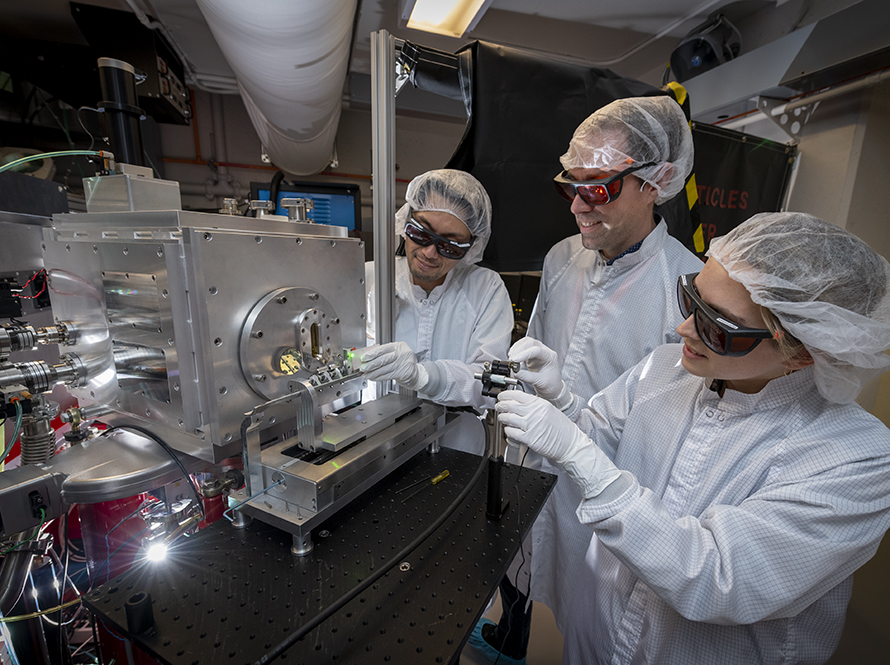 Three researchers, gowned and goggled for a laser area, work on a biomedical application of laser plasma accelerators