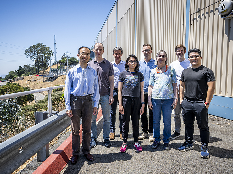 A group of ATAP researchers and staff outside a superconducting magnet facility with a scenic view in the background