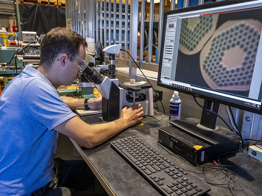 Researcher uses a microscope connected to a large computer monitor to examine details of a cross section of a superconducting wire