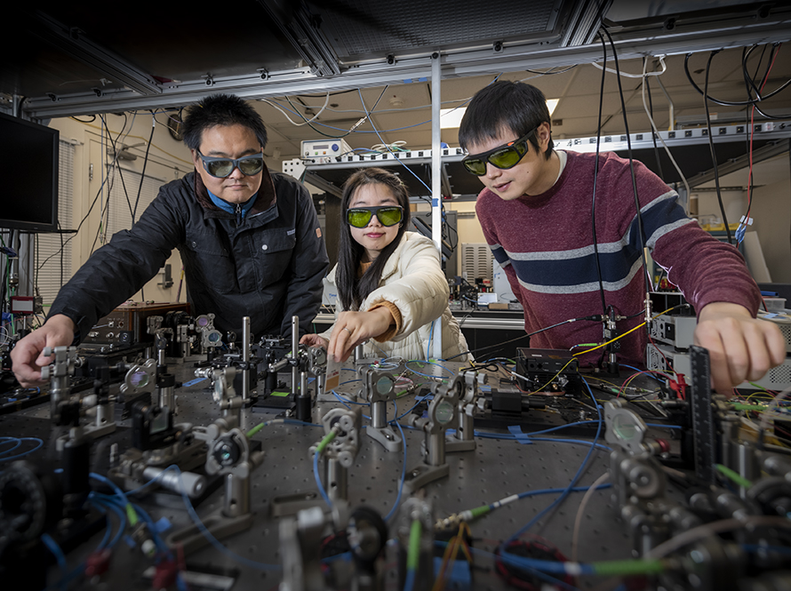 Three researchers in laser goggles at an optical bench